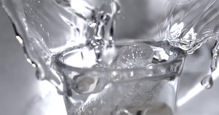 Ice cube falling over a cup of water and water splashing around indoors