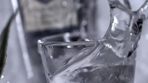 In an extreme closeup slowmotion shot an ice cube is dropped into a glass creating a dramatic splash that sends water everywhere