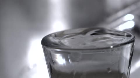 Close up of a water droplet falling into a glass cup filled with water