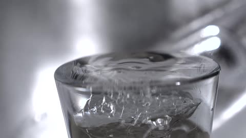 The video shows a closeup shot of a clear glass being filled with water from a faucet the water is shown splashing and overflowing from the top of the glass the words filmsupply are visible as a watermark on the video