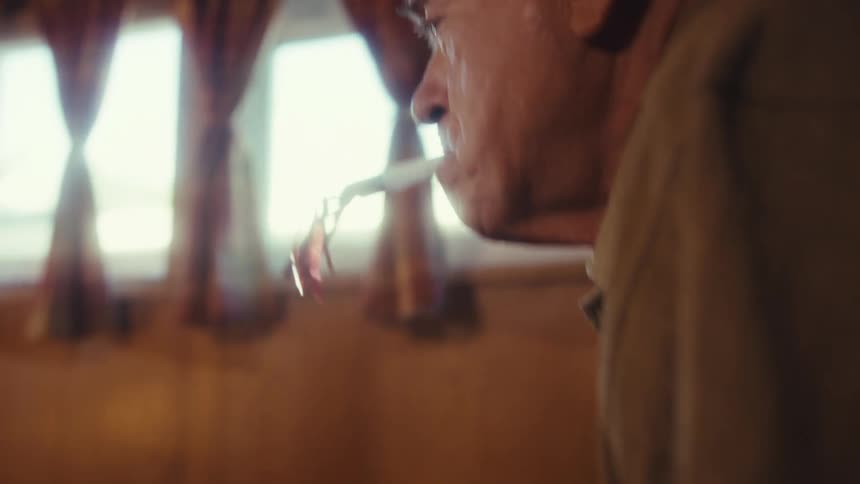 Elderly man wearing a party hat walking and carrying a present on his hands while blowing into a party whistle indoors during day time