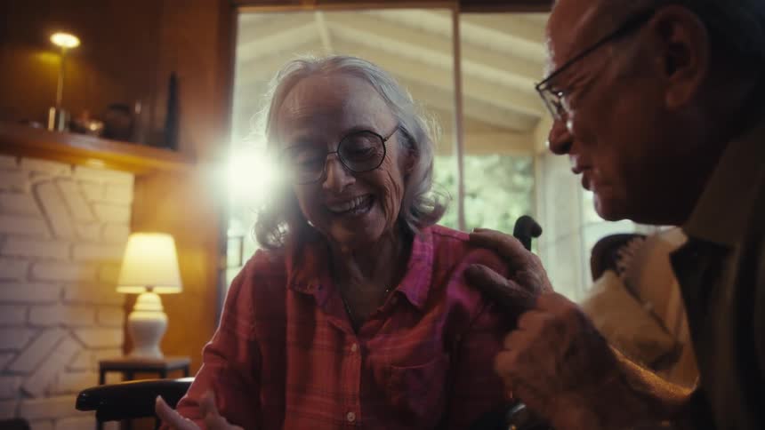 An elderly couple smiles and enjoys time together inside a cozy home
