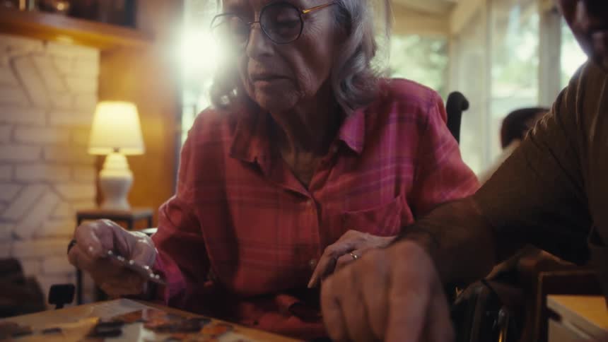Elderly man and woman playing with a jigsaw puzzle over a wooden table indoors during day time