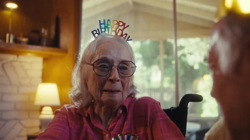 Smiling elderly woman with a happy birthday headband celebrates next to a man