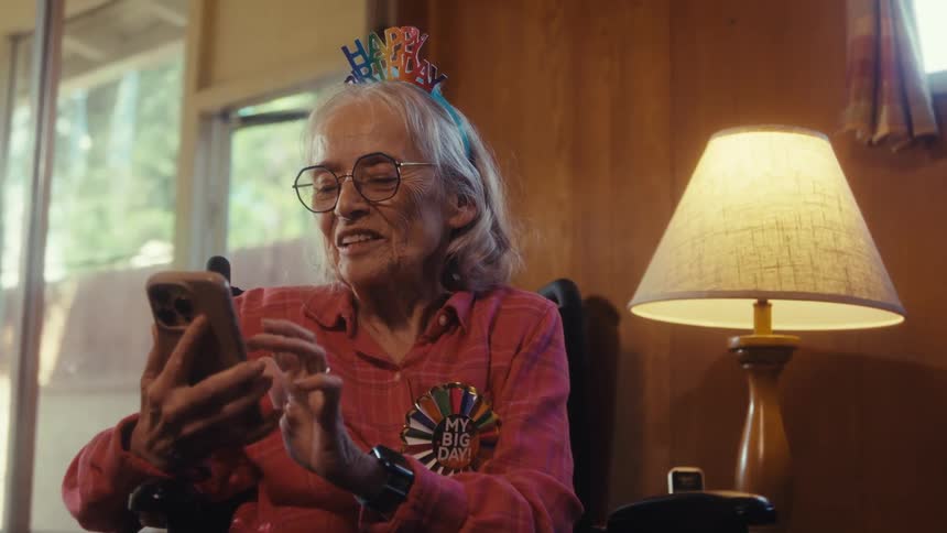 Elderly woman smiling at her phone indoors during a birthday