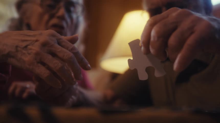 Elderly couple fitting a puzzle piece together indoors