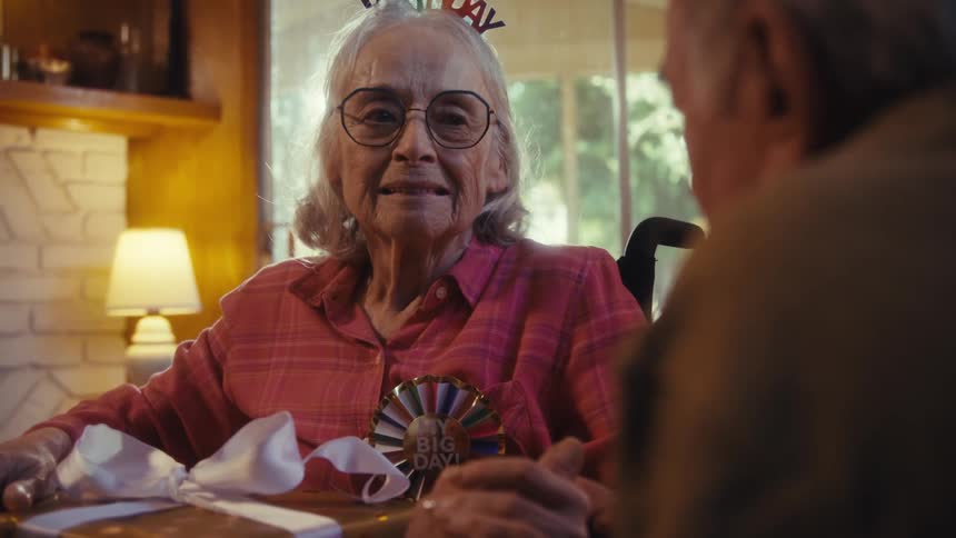 An elderly woman gets emotional after receiving a gift from her partner in the living room