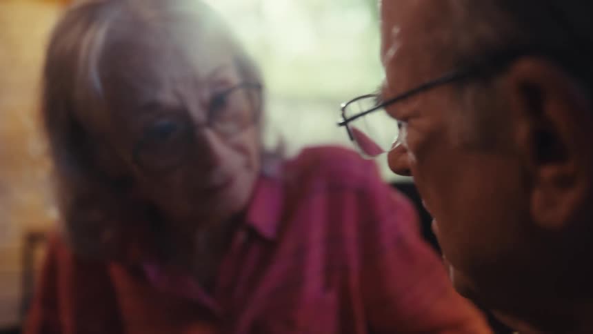 Close up portrait of an elderly man and woman conversing while sitting together indoors during daytime