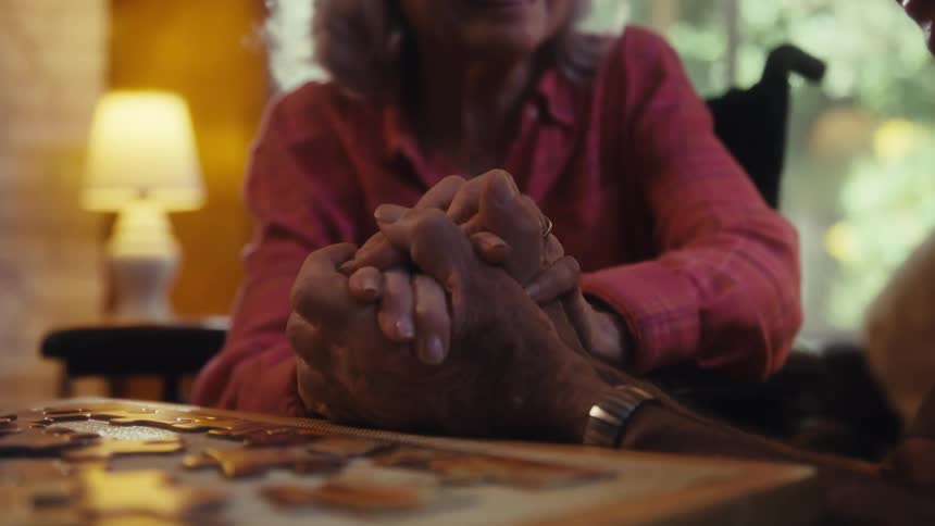 Elderly man and woman talking while smiling and holding each others hands indoors during day time