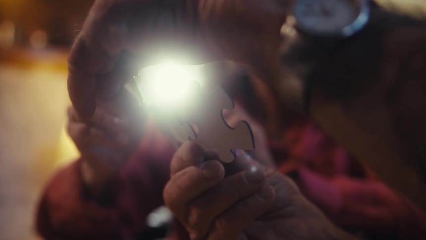 Elderly hands hold puzzle piece illuminated by light