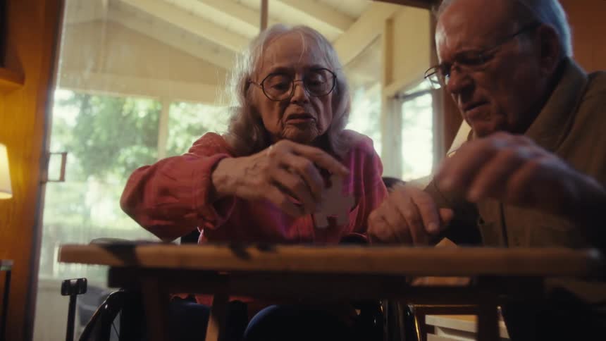 Elderly couple focuses on assembling a puzzle on the table