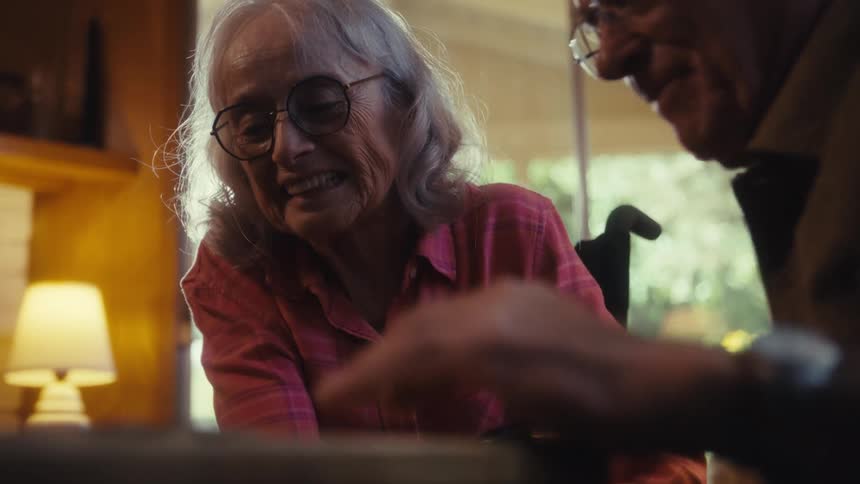 Smiling an elderly woman leans over a small puzzle table fully engaged