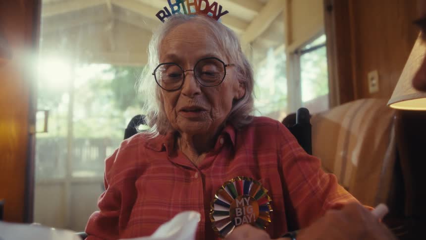 Elderly woman laughing and talking with an elderly man wearing party hats with birthday theme indoors during day time