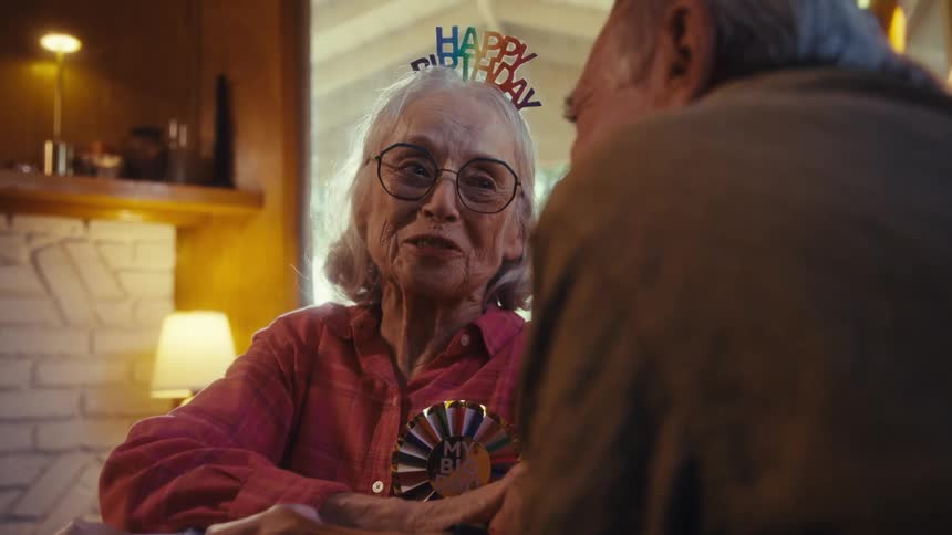 Wearing a birthday crown an elderly woman hugs an elderly man