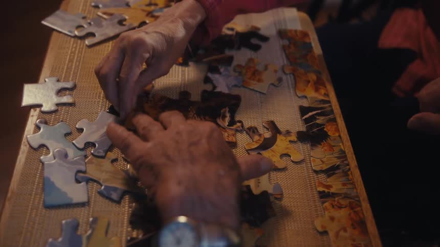 Close up of an elderly man and woman arranging a jigsaw puzzle on a table indoors