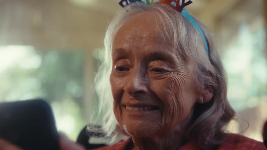 An elderly woman shows emotion while talking on a video call indoors