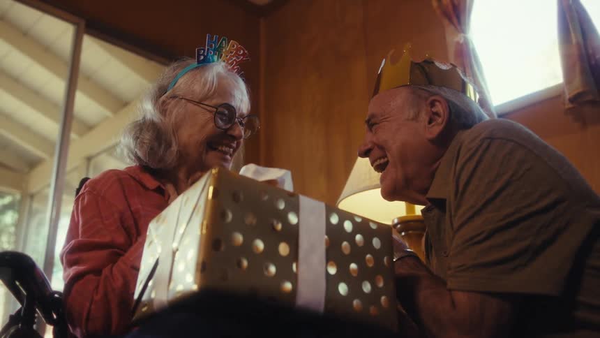 An elderly couple laughs while celebrating a birthday indoors