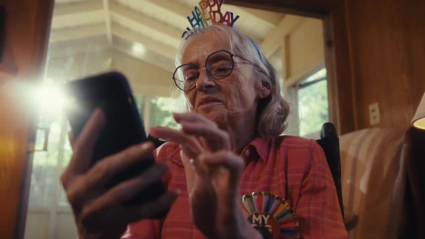 Close up of an elderly woman using a mobile phone while sitting in a living room during daytime