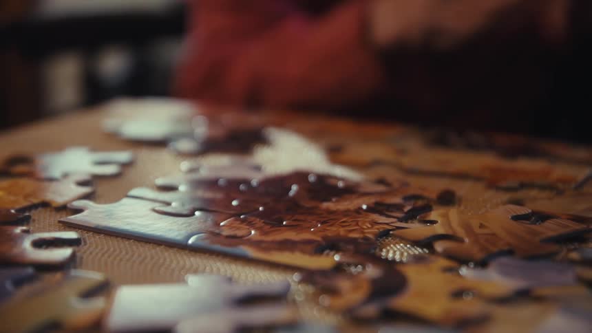 Elderly hands adjust pieces of a colorful puzzle on the table