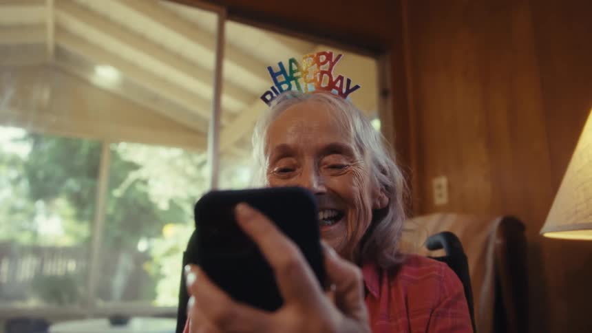 An elderly woman smiles as she holds her smart phone while talking