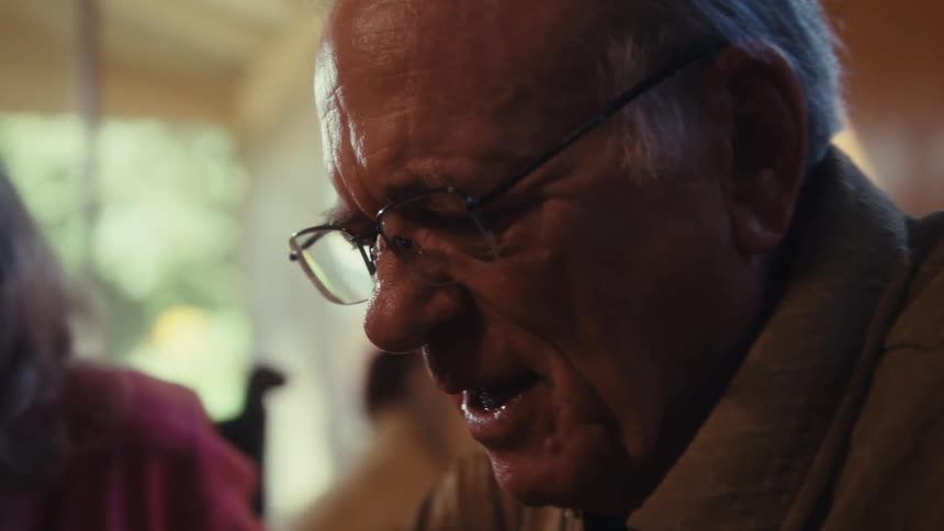 An elderly couple wearing glasses playing a board game in the living room at midday