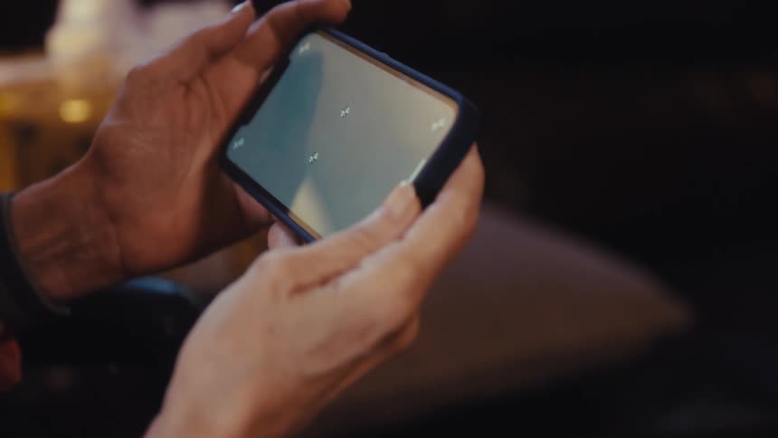 Close up of an elderly woman watching media content on a mobile phone while sitting in a room during daytime