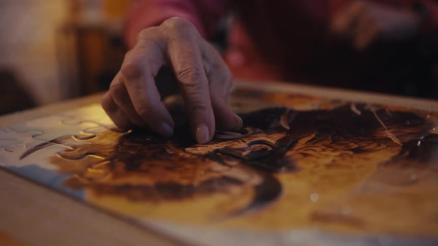 Close up of an elderly woman fitting the last piece of a jigsaw puzzle on a table indoors
