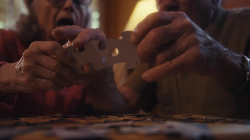 An elderly couple plays a puzzle game together at a table