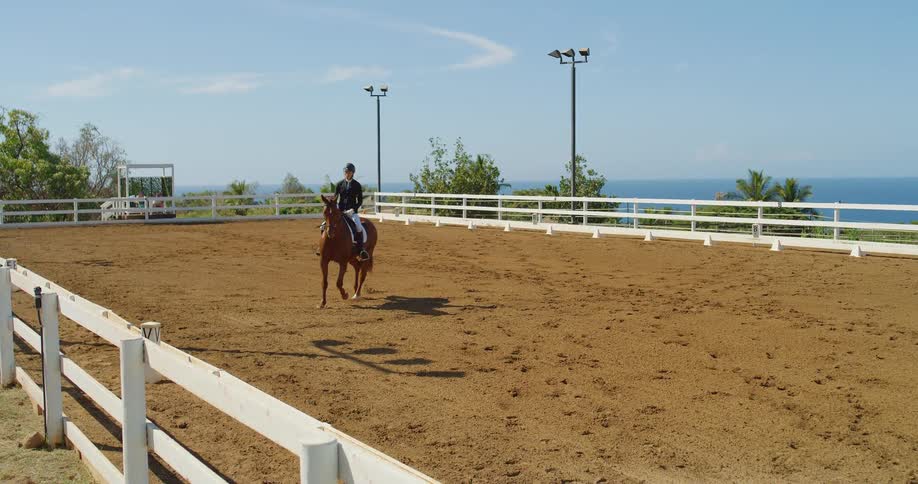Horse rider guides their trotting horse across a corral located near the coast on a slightly cloudy day