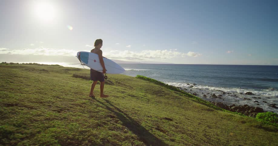 Surfer walks barefoot on cliffs carrying a surfboard toward the ocean