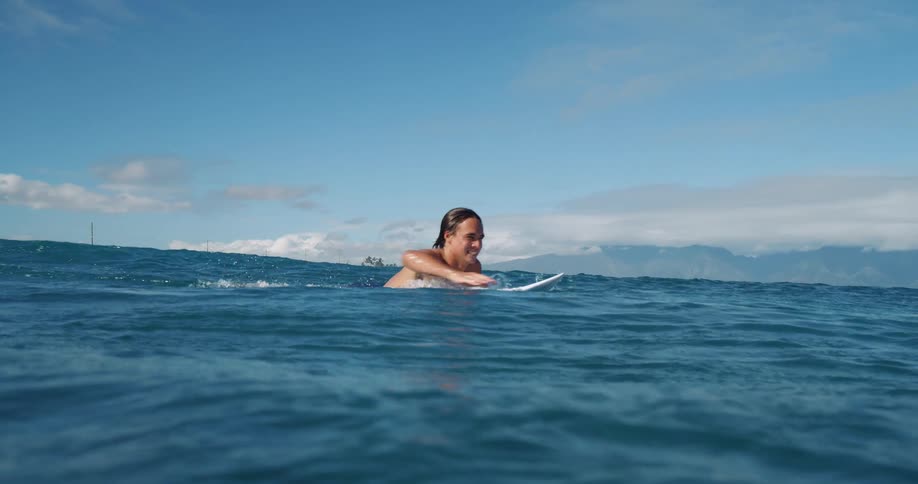 White man lying on a surfboard and swimming into the sea with a beach far away on the background outdoors during day time