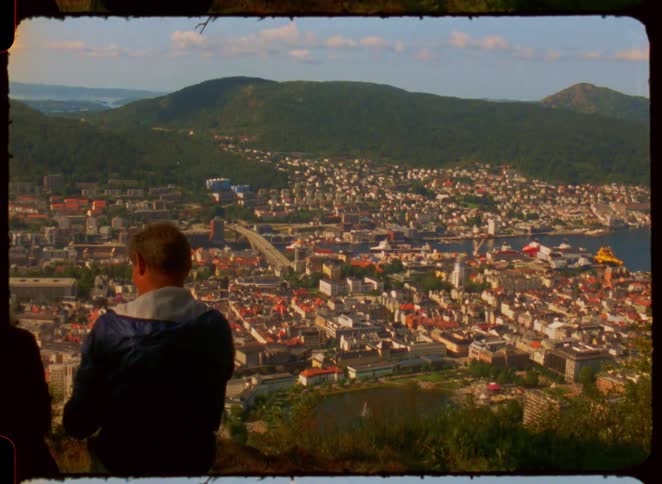 Men watch from above the panoramic view of a city surrounded by mountains
