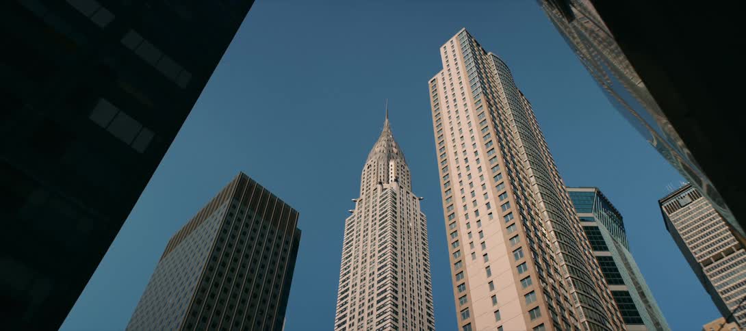 A lowangle shot from a city street looks up at the iconic chrysler building and surrounding skyscrapers against a clear blue sky