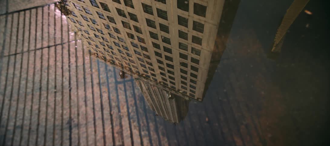 The reflection of a tall building can be seen in a puddle of water