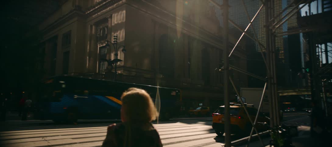 A woman waiting to cross a city street watches multiple vehicles pass by
