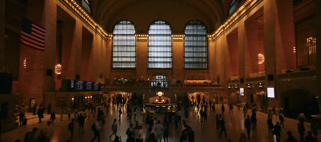 The video shows the bustling main concourse of grand central terminal in new york city people are walking around the large open space and a large foursided clock is visible in the center the halls iconic beauxarts architecture is prominent wit