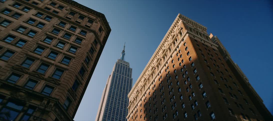 View looking up at the empire state building between tall buildings
