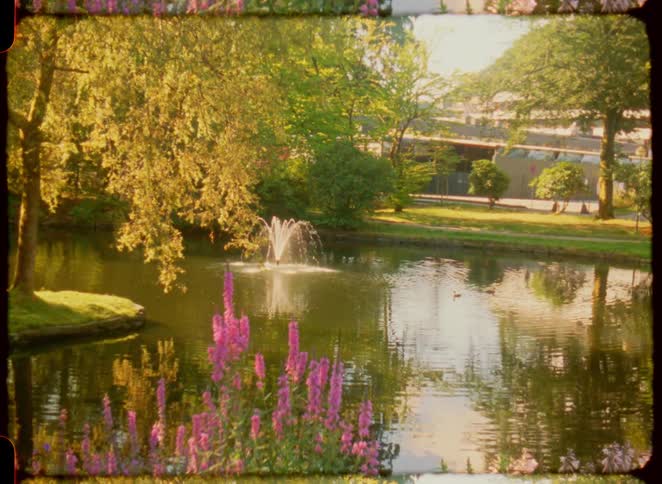 Park lake with a fountain in the center surrounded by trees and purple flowers