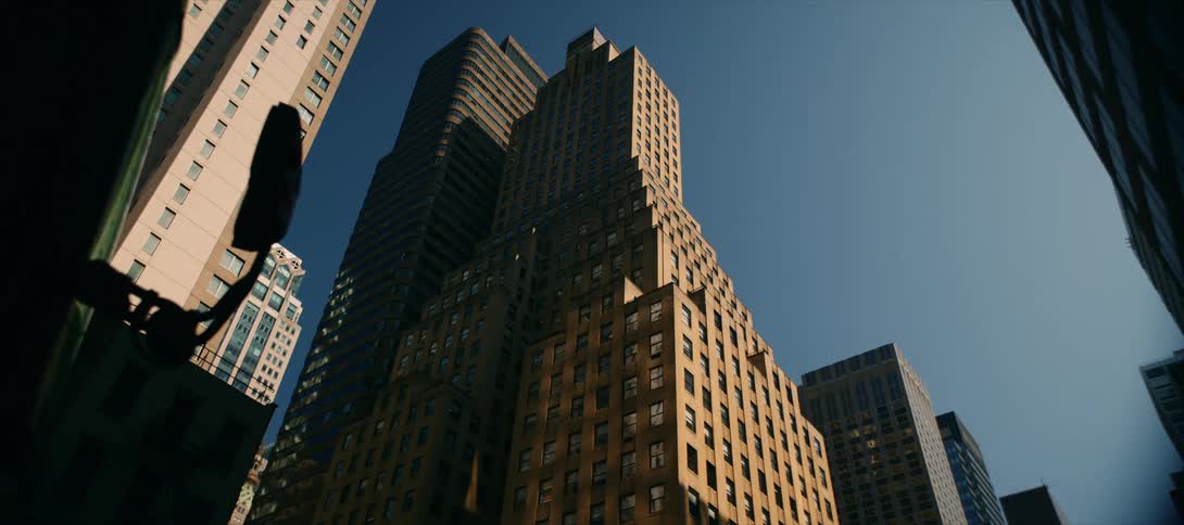 The video shows an upwardangle shot of a couple of tall tancolored office buildings in a city the camera slowly pans upward revealing the clear blue sky