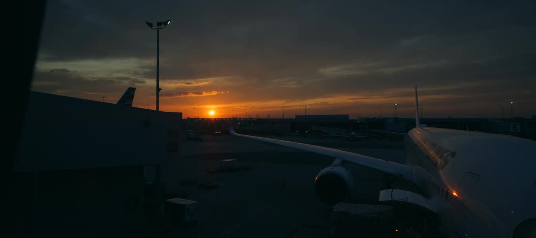 An airplane is parked at an airport during a dramatic sunset with clouds in the sky