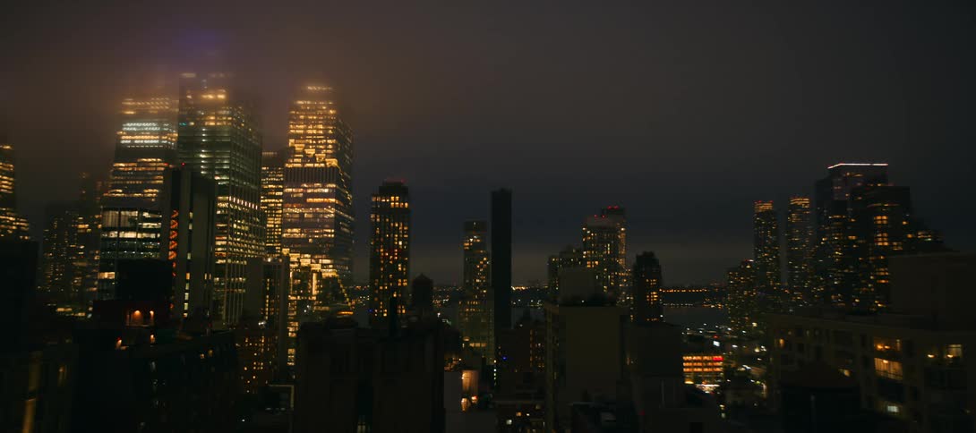 A city skyline glows at night with tall skyscrapers under a cloudy sky