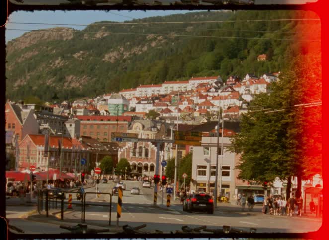 Busy street with cars and pedestrians surrounded by redroofed houses and mountains in the background