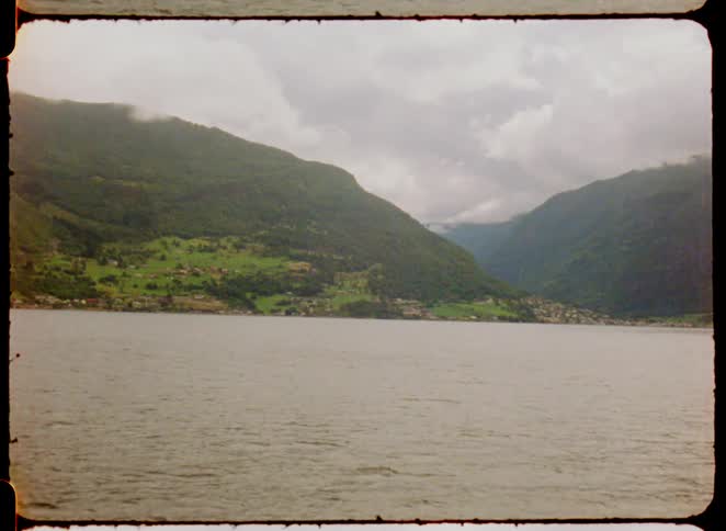 Green mountains surround a lake under a cloudy sky