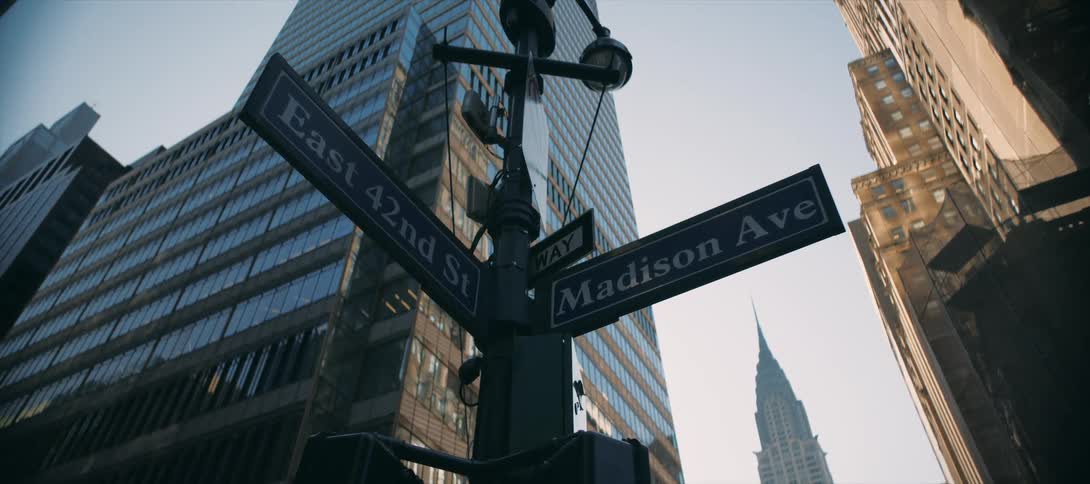 Iconic midtown street signs point up at towering skyscrapers in clear light