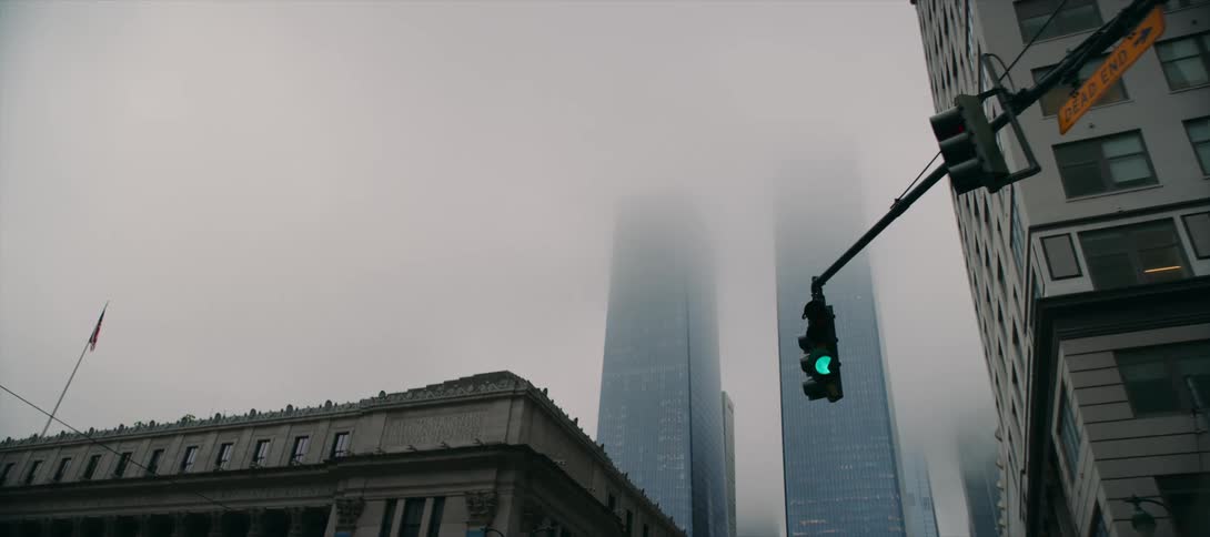 Tall city buildings fade into fog with a red traffic light in the foreground