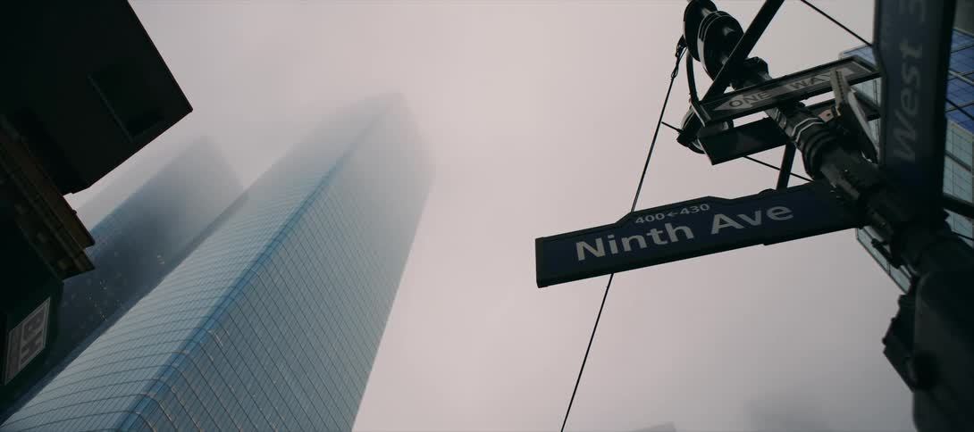 Ninth avenue street sign in the foreground with a skyscraper covered in fog in the background