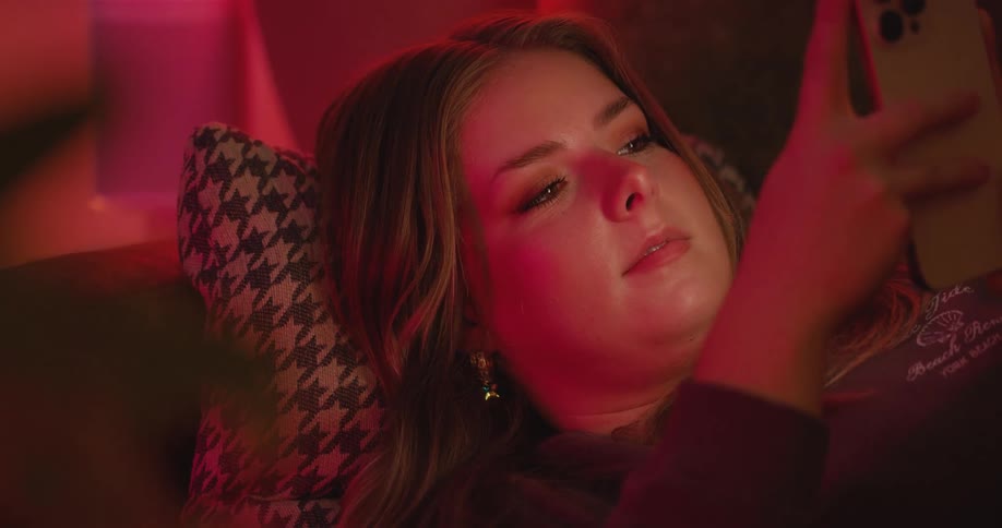 Close up of a young woman using a mobile phone while lying down in a red lit room