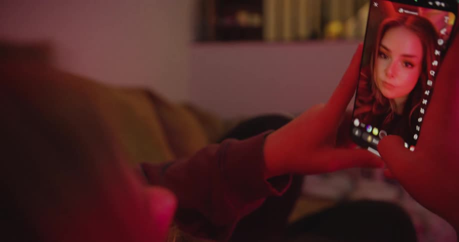 Woman lying on the couch taking a selfie with a face filter on the cellphone