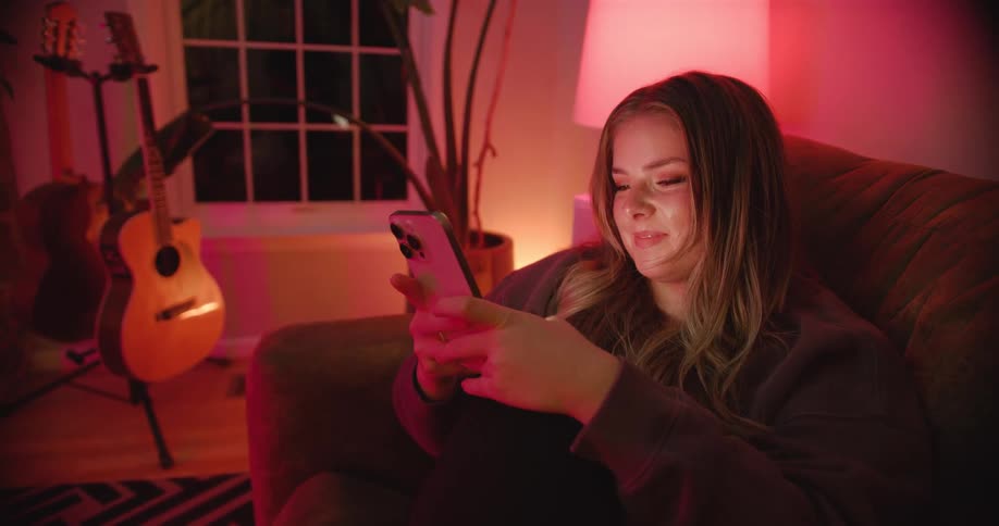 A young woman sitting on a couch smiles while using her smart phone