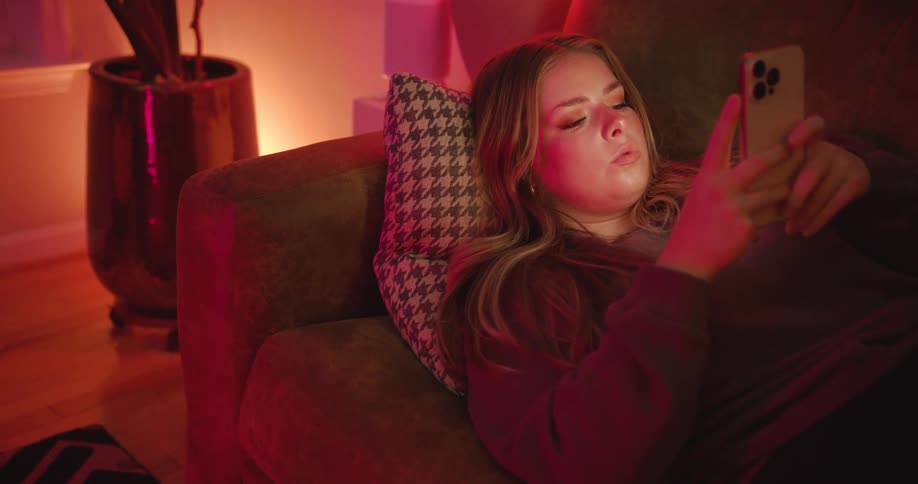 Woman lying on the sofa at night interacting with her smartphone
